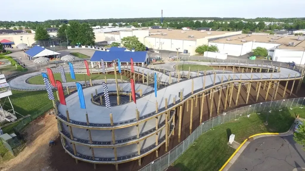 Elevated multi-level go-kart track on timber pilings with race flags, seen from a drone