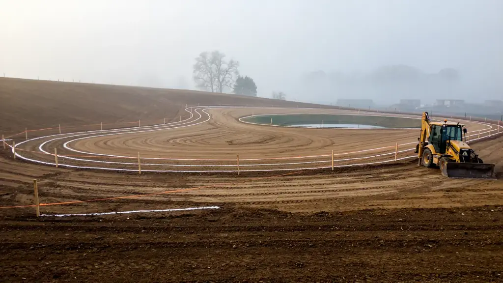 Graded lot with survey stakes and string lines marking the curve of a future track and a pond